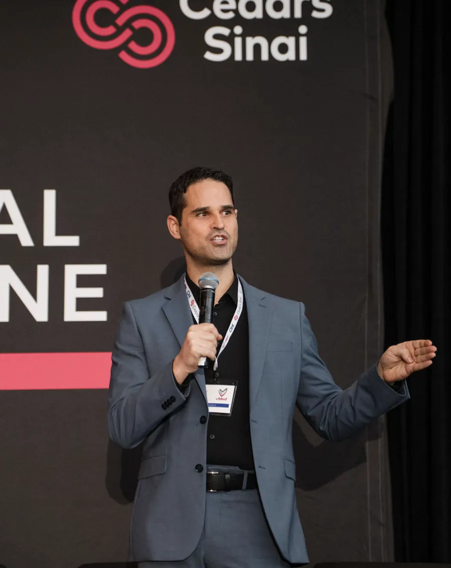 Omer Liran speaking on stage in front of a Cedars-Sinai banner